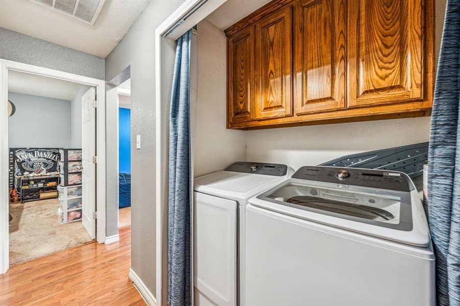 Clothes washing area with cabinets, light wood-type flooring, and separate washer and dryer