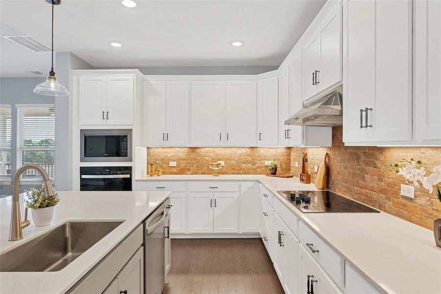 Huge kitchen with lots of cabinets, large island, quartz countertops, and attractive brick backsplash.