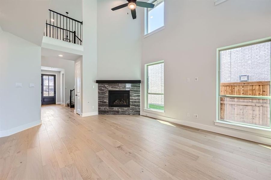 Unfurnished living room with light hardwood / wood-style flooring, a fireplace, ceiling fan, and a high ceiling