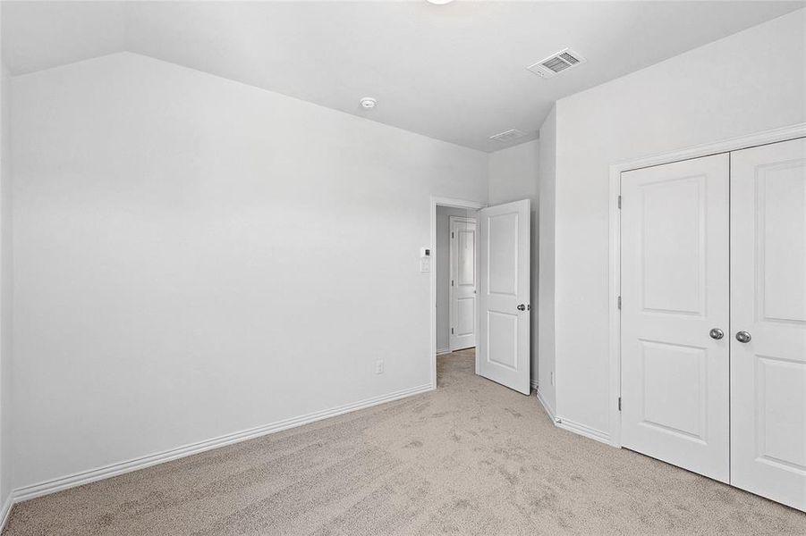 Unfurnished bedroom with light carpet, a closet, and vaulted ceiling