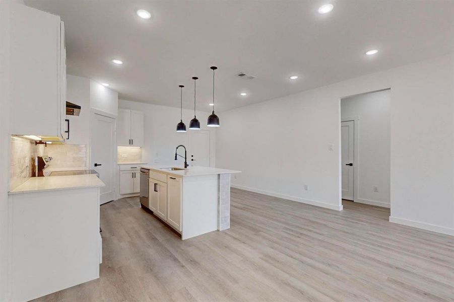 Kitchen featuring tasteful backsplash, white cabinets, sink, light hardwood / wood-style flooring, and a kitchen island with sink