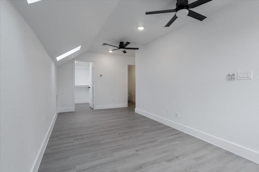 Additional living space featuring light hardwood / wood-style flooring, lofted ceiling with skylight, and ceiling fan