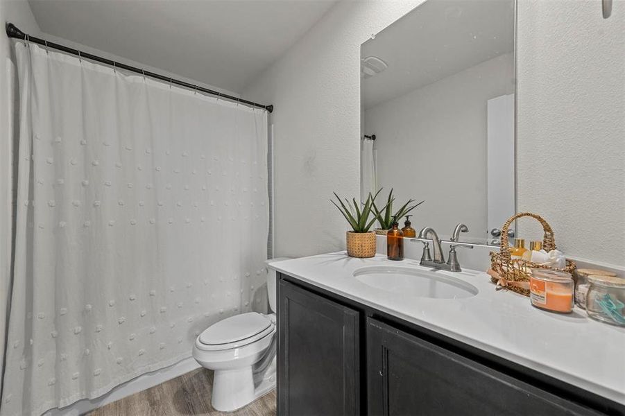 Full bathroom with vanity, toilet, shower / bathtub combination with curtain, and hardwood / wood-style floors