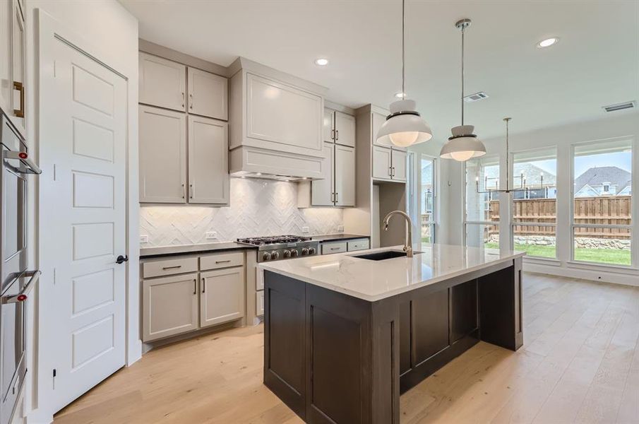 Kitchen featuring tasteful backsplash, light hardwood / wood-style flooring, gas range, premium range hood, and sink