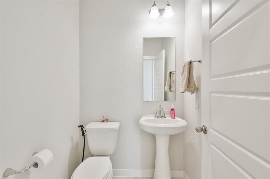 This is a clean, compact half-bathroom featuring a pedestal sink, toilet, and a mirror with overhead lighting.
