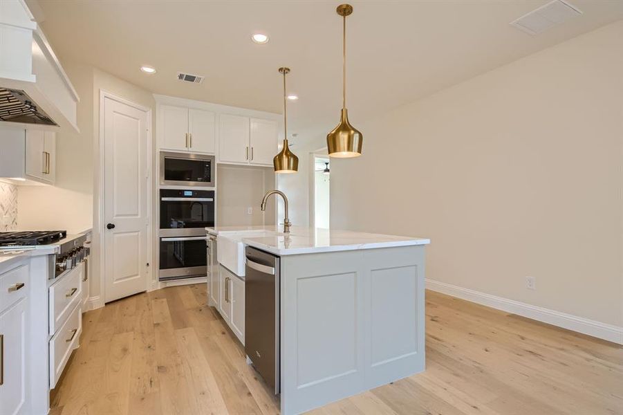 Kitchen featuring an island with sink, light wood-type flooring, white cabinetry, and hanging light fixtures