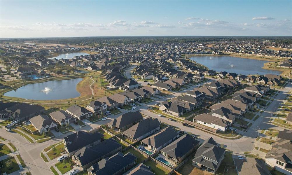 This aerial photo showcases a sprawling suburban neighborhood with uniform houses and manicured lawns, featuring a central lake with a fountain, likely offering a serene living environment.