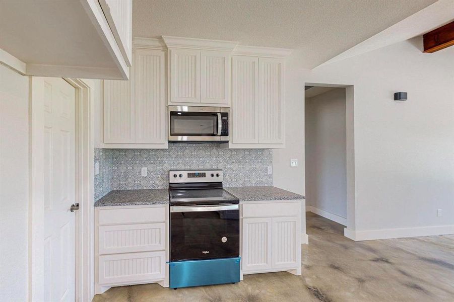 Kitchen with appliances with stainless steel finishes, light stone countertops, backsplash, and white cabinetry