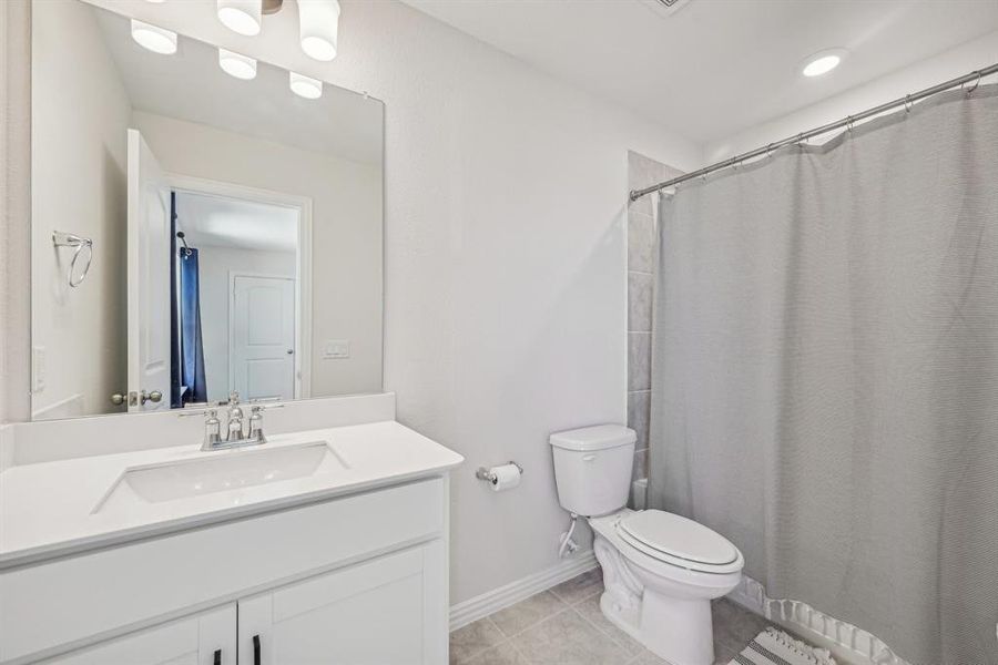 Ensuite bathroom in upstairs bedroom  featuring vanity, curtained shower, tile patterned flooring, and toilet