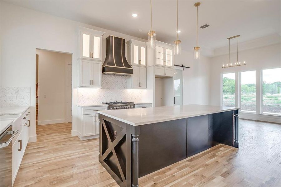 Kitchen featuring premium range hood, white cabinets, a center island, light hardwood / wood-style floors, and backsplash