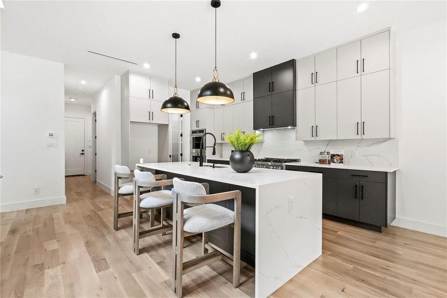 Kitchen featuring hanging light fixtures, backsplash, a kitchen island with sink, light wood-type flooring, and sink