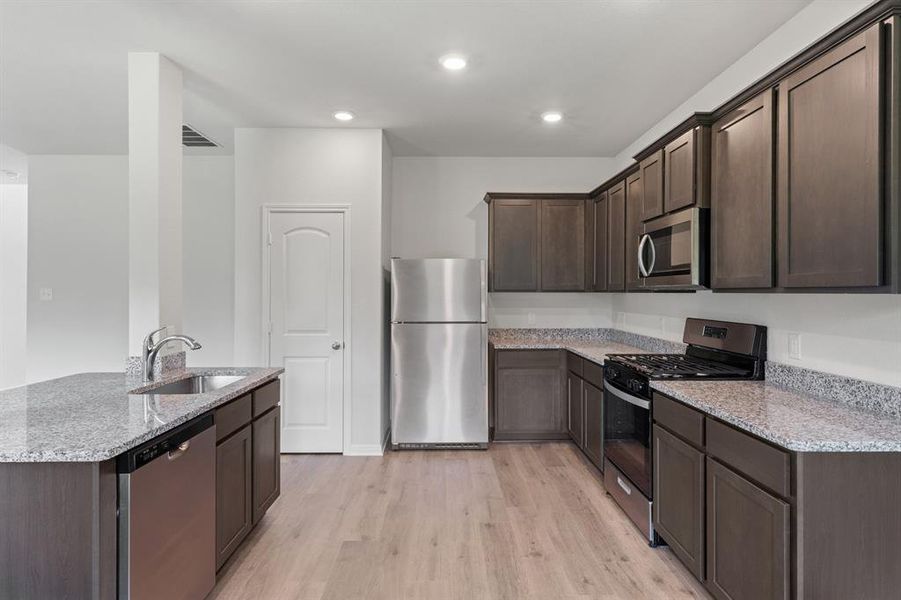 Kitchen featuring light hardwood / wood-style flooring, light stone countertops, stainless steel appliances, sink, and dark brown cabinets