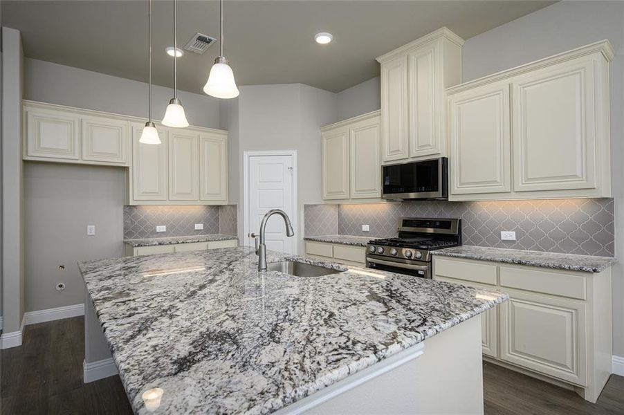 Kitchen featuring decorative backsplash, appliances with stainless steel finishes, and an island with sink
