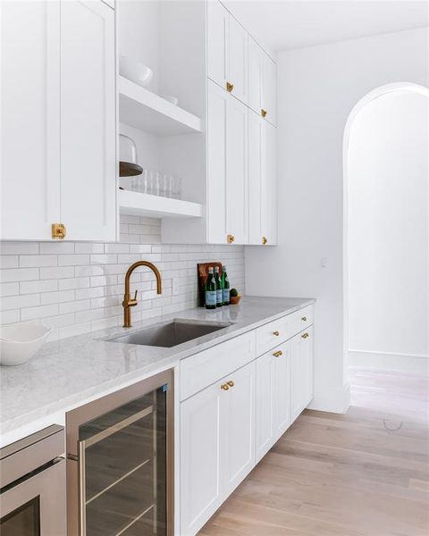 Bar with wine cooler, sink, white cabinetry, and light stone counters