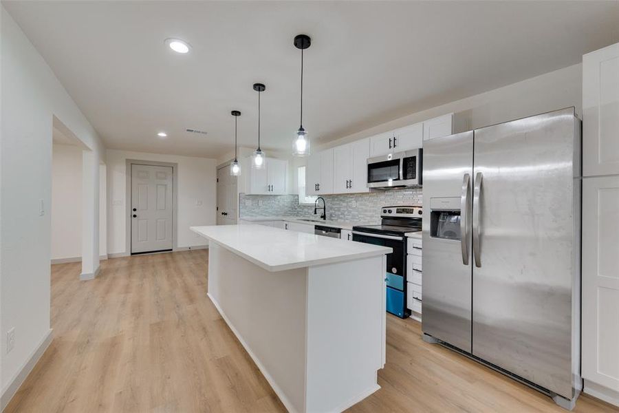 Kitchen with light hardwood / wood-style flooring, stainless steel appliances, white cabinets, backsplash, and pendant lighting
