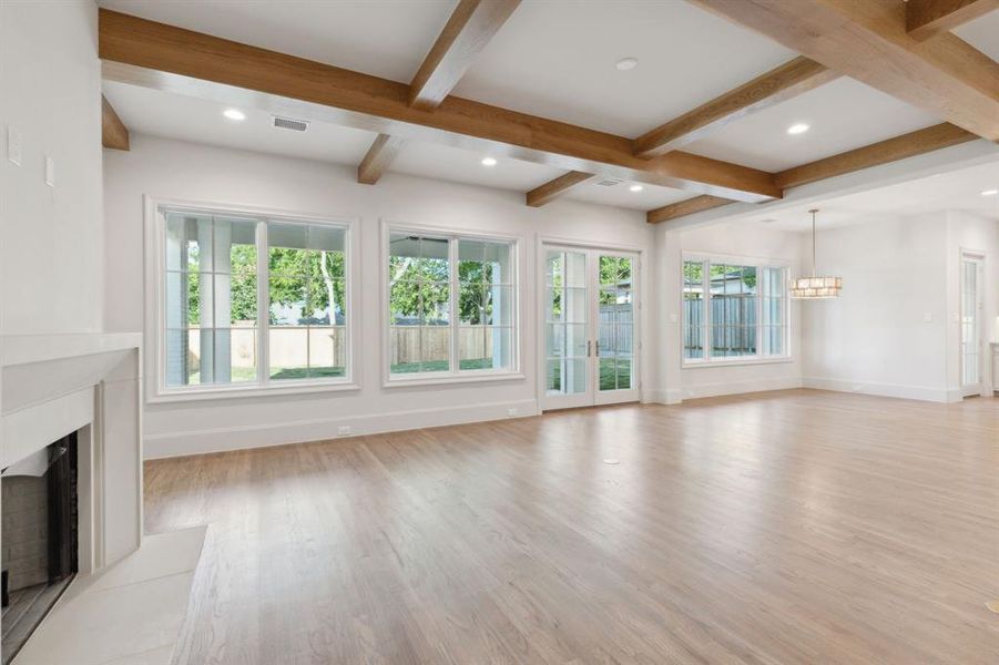Unfurnished living room with light hardwood / wood-style floors, a notable chandelier, and beamed ceiling