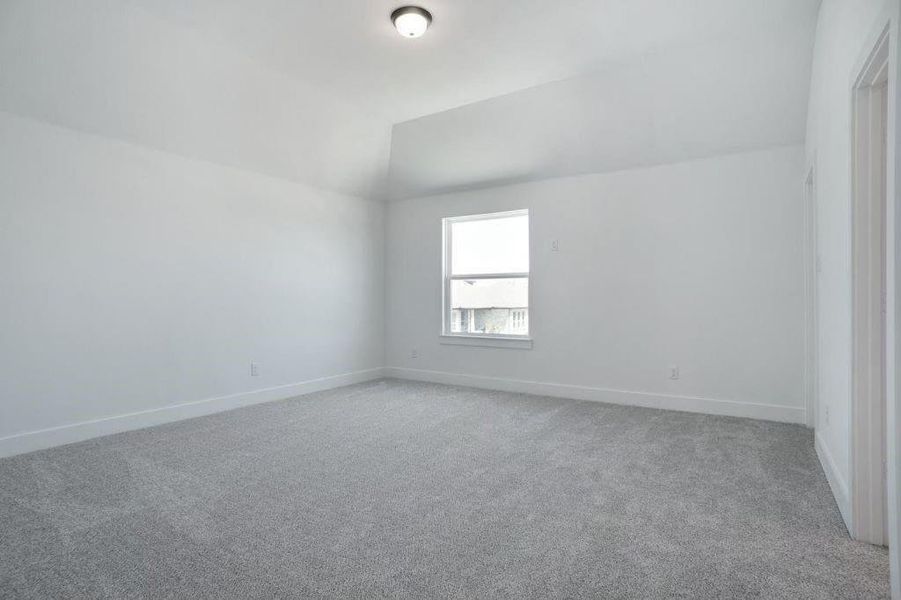 Empty room with vaulted ceiling and light colored carpet