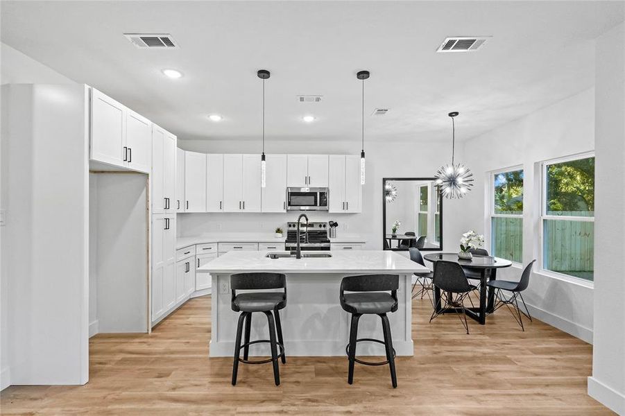 Kitchen with white cabinets, an island with sink, light hardwood / wood-style flooring, and decorative light fixtures