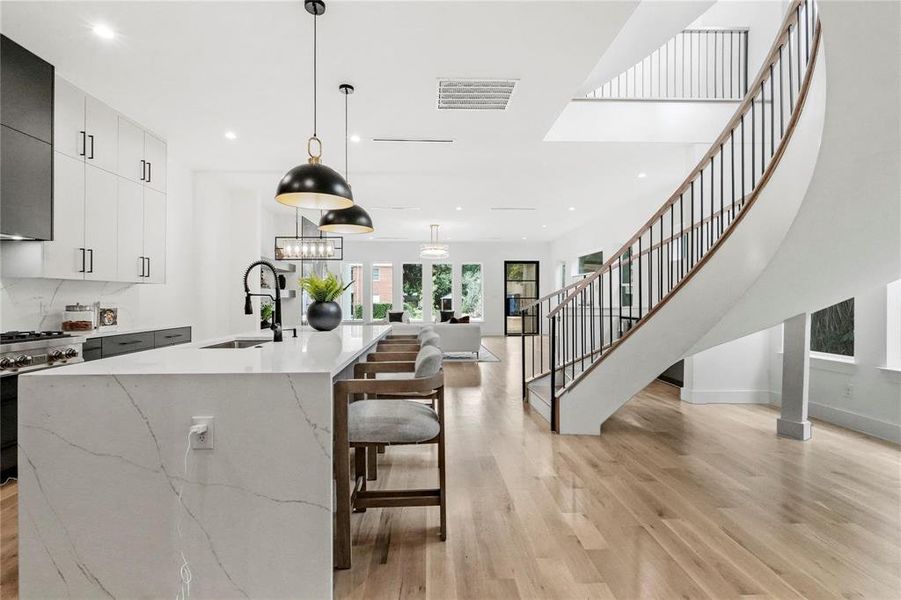 Kitchen with a large island, hanging light fixtures, high end white range oven, light hardwood / wood-style flooring, and sink