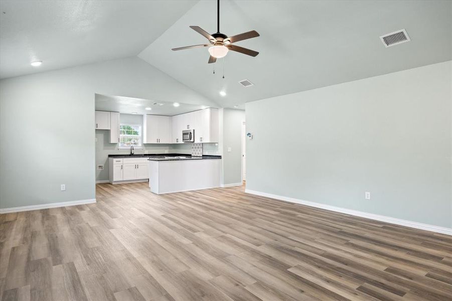 Unfurnished living room with high vaulted ceiling, ceiling fan, and light hardwood / wood-style floors