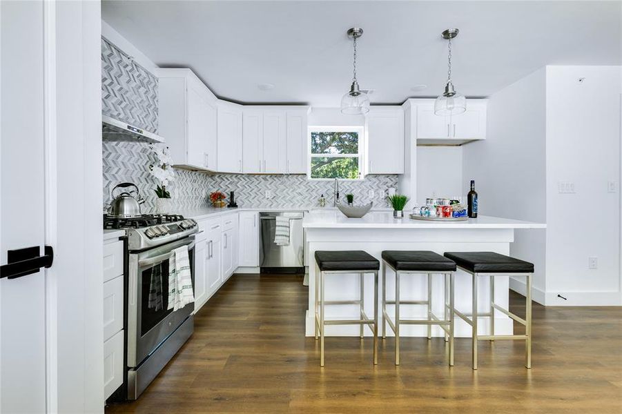 Kitchen featuring dark hardwood / wood-style flooring, hanging light fixtures, white cabinetry, and stainless steel appliances