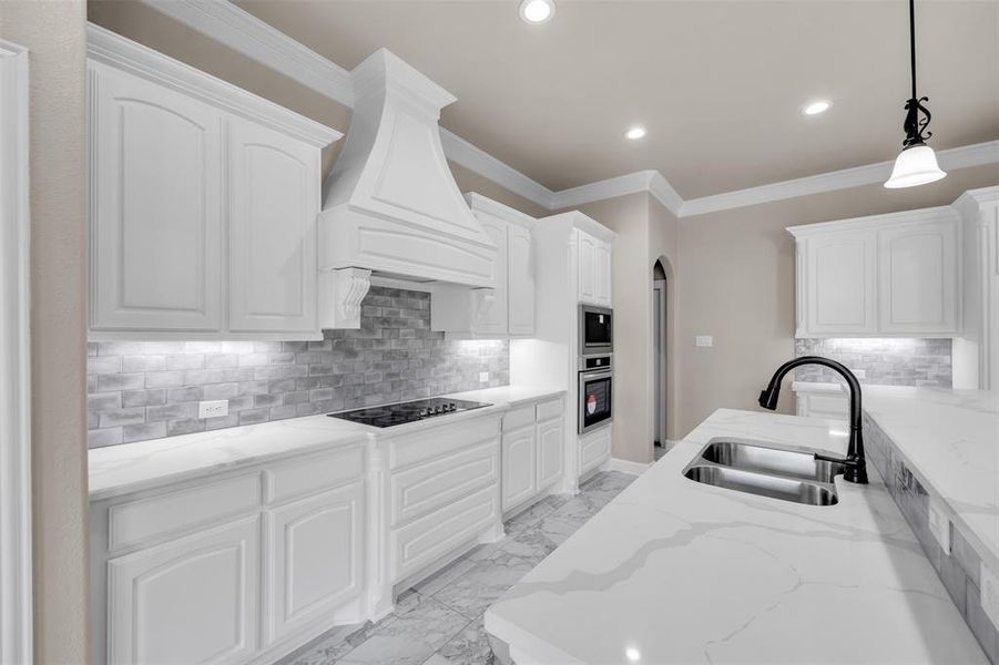 Kitchen featuring light stone counters, stainless steel appliances, white cabinetry, custom range hood, and sink