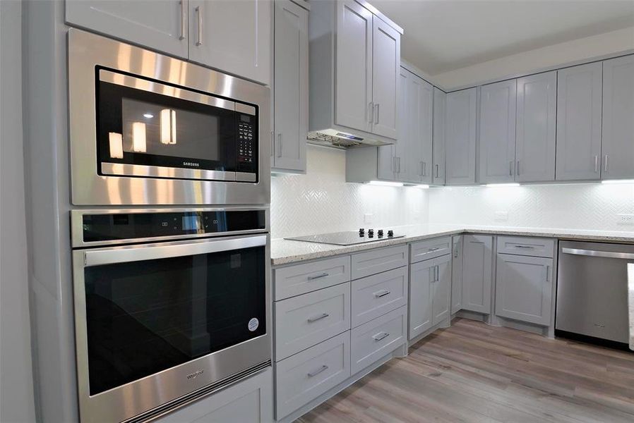 Kitchen with light hardwood / wood-style floors, light stone counters, tasteful backsplash, stainless steel appliances, and wall chimney range hood