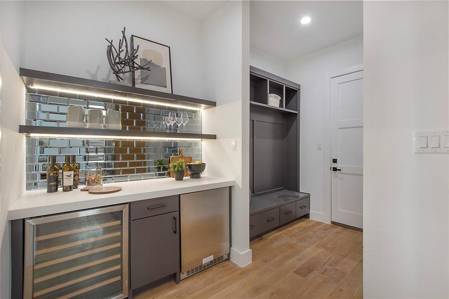 Bar with stainless steel refrigerator, tasteful backsplash, wine cooler, and light hardwood / wood-style flooring