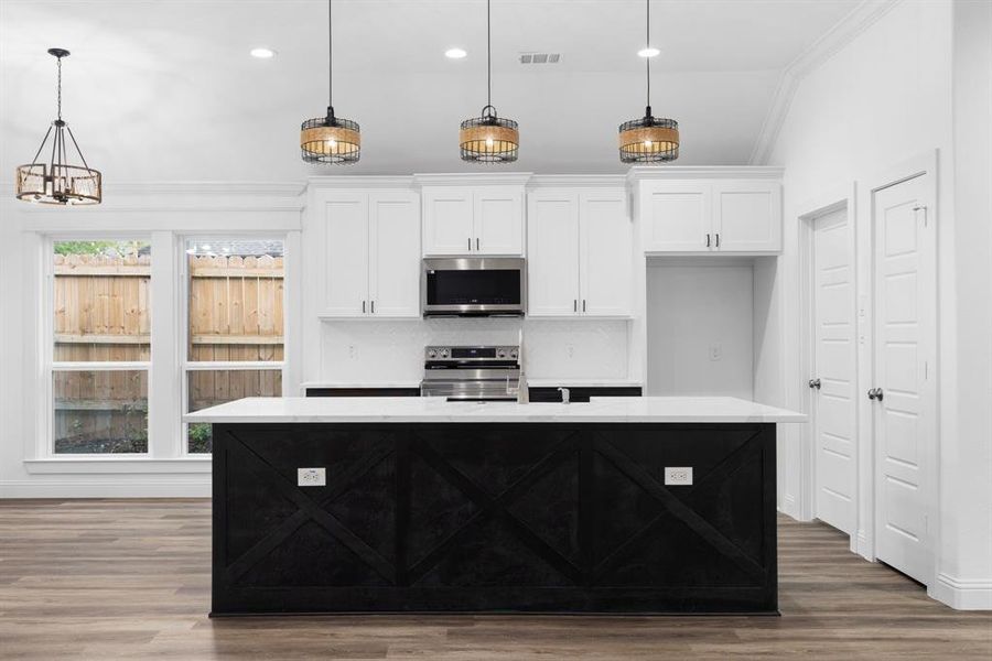 Kitchen featuring white cabinetry, appliances with stainless steel finishes, a kitchen island with sink, and decorative light fixtures