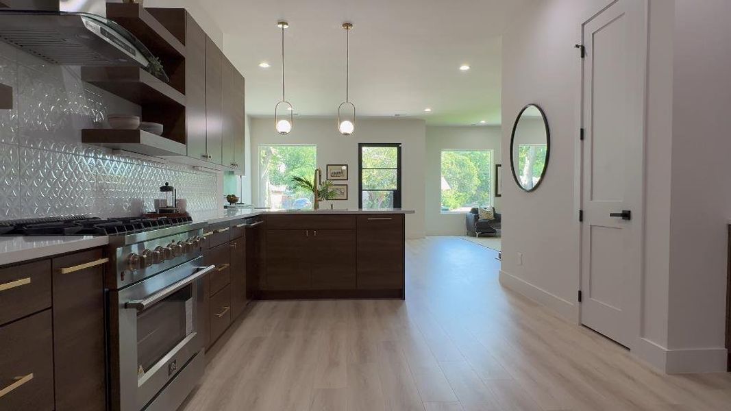 Kitchen with kitchen peninsula, hanging light fixtures, light hardwood / wood-style floors, decorative backsplash, and high end stove