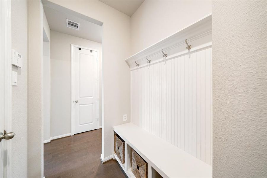 This is a tidy entryway with a built-in bench and storage cubbies beneath, complemented by a row of hooks above for hanging coats or bags. The space features neutral colors and the same wood flooring throughout! Ideal for organizing outerwear and shoes.