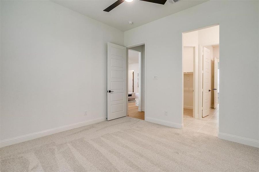 Unfurnished bedroom with a closet, a walk in closet, ceiling fan, and light colored carpet