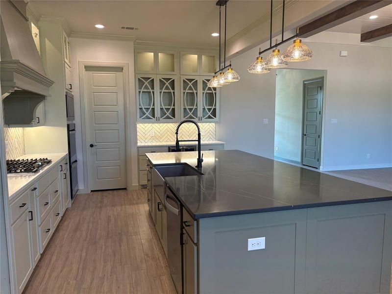 Kitchen featuring an island with sink, beam ceiling, wood-type flooring, decorative light fixtures, and custom range hood