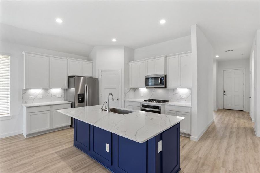 Features include granite countertops paired with a coordinating backsplash, stainless steel appliances, crisp white cabinets, under cabinet lighting, recessed lighting, and a sprawling island with breakfast bar seating.