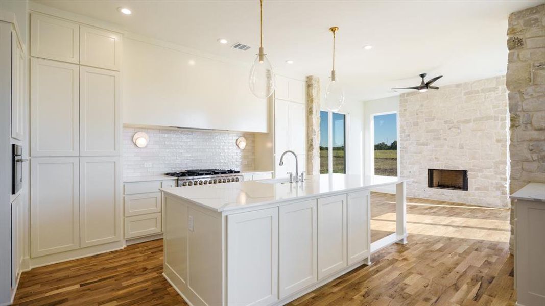 Kitchen with tasteful backsplash, light stone counters, light hardwood / wood-style flooring, sink, and decorative light fixtures