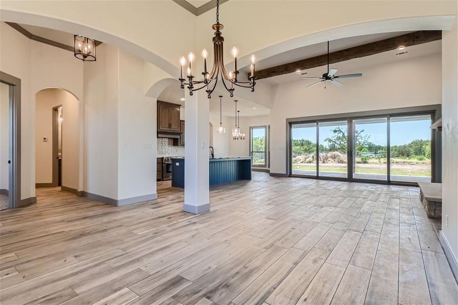 Unfurnished living room featuring beam ceiling, ceiling fan with notable chandelier, a towering ceiling, and light hardwood / wood-style flooring