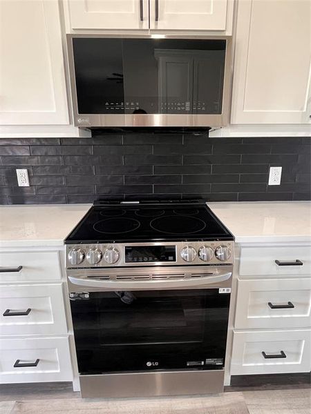 Kitchen with backsplash, stainless steel range, and white cabinets