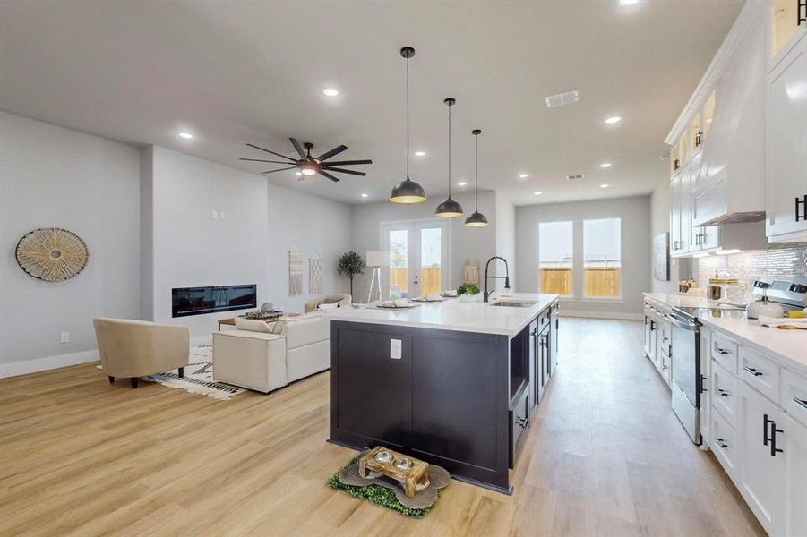 Kitchen with electric range, decorative light fixtures, light hardwood / wood-style flooring, and a center island with sink