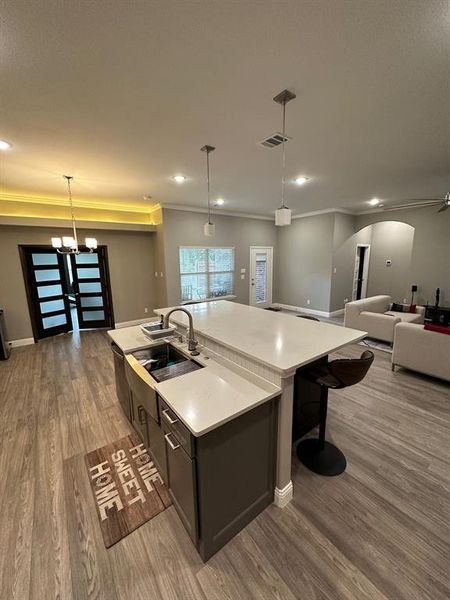 Kitchen with decorative light fixtures, hardwood / wood-style floors, sink, and a kitchen island with sink