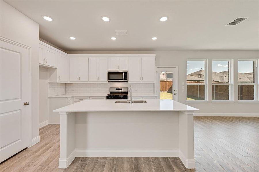 Kitchen featuring decorative backsplash, stainless steel appliances, white cabinetry, and sink