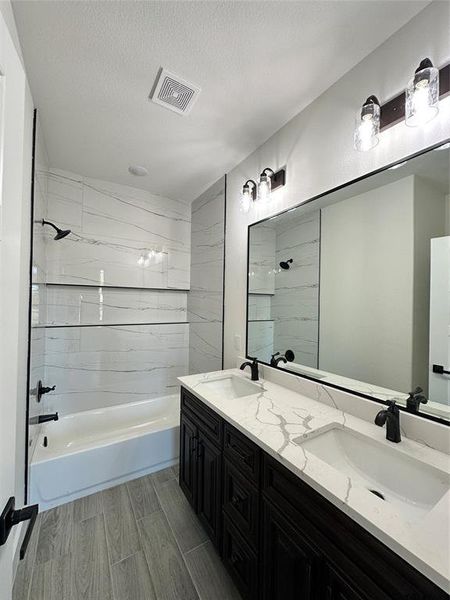 Bathroom featuring wood-type flooring, a textured ceiling, vanity, and tiled shower / bath