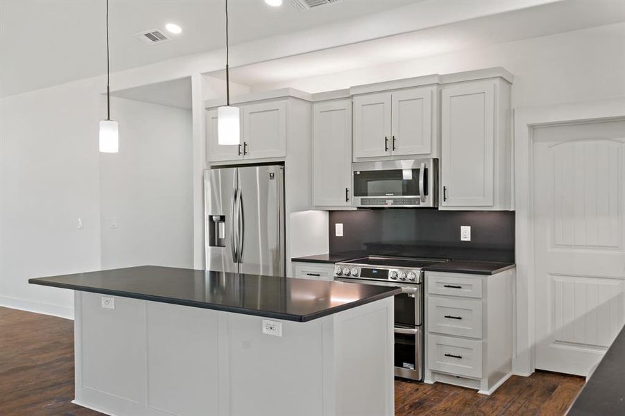 Kitchen with dark wood-type flooring, stainless steel appliances, decorative light fixtures, and white cabinets