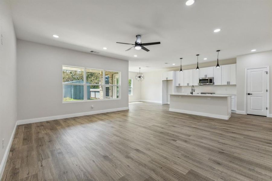 Unfurnished living room featuring ceiling fan with notable chandelier, light hardwood / wood-style floors, and sink