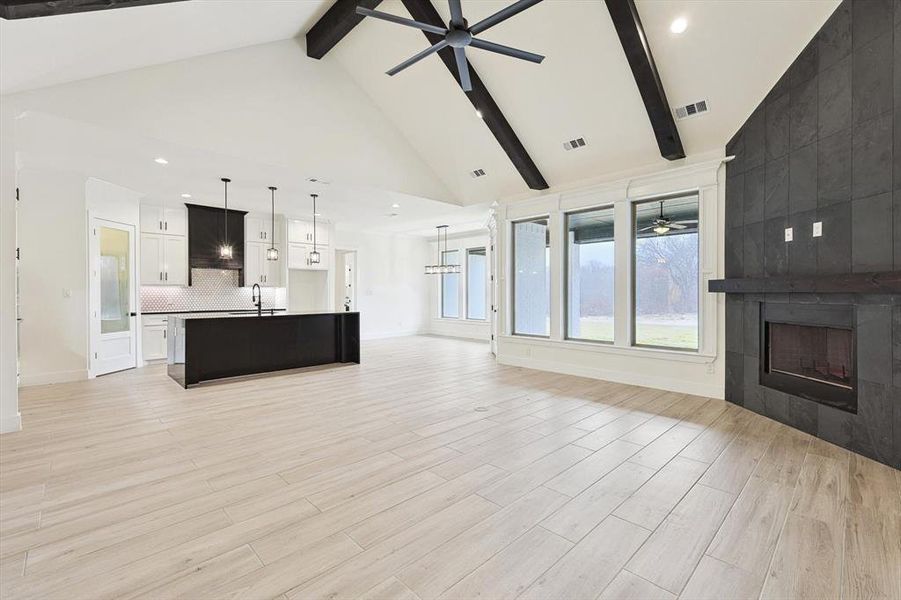 Unfurnished living room featuring light wood-type flooring, beamed ceiling, a fireplace, high vaulted ceiling, and ceiling fan