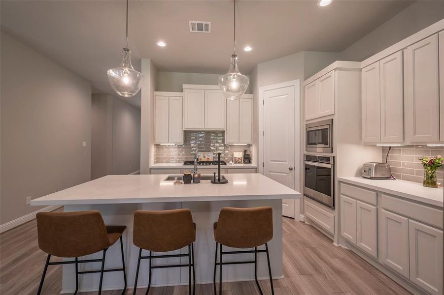 A timeless classic look kitchen with white cabinets, grey tone subway tile backsplash, under cabinet lighting and Quartz countertops.