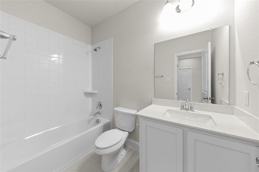 Full bathroom featuring tile flooring, large vanity, toilet, and tiled shower / bath combo