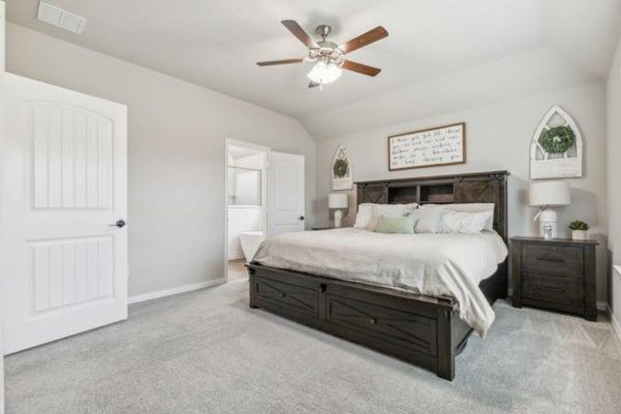 Bedroom with vaulted ceiling, light colored carpet, ensuite bath, and ceiling fan