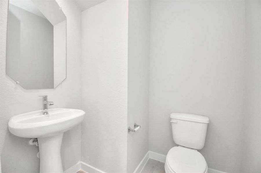 This half bathroom features a stylish pedestal sink, modern hardware, and bright recessed lighting, creating a sleek and inviting space. Sample photo of completed home with similar floor plan. Actual colors and selections may vary.