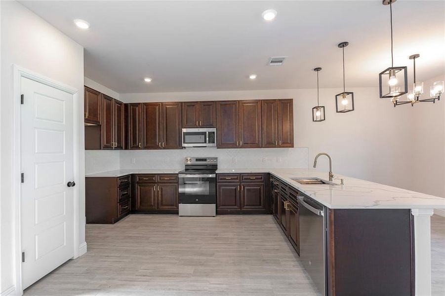 Kitchen featuring kitchen peninsula, dark brown cabinets, sink, pendant lighting, and stainless steel appliances