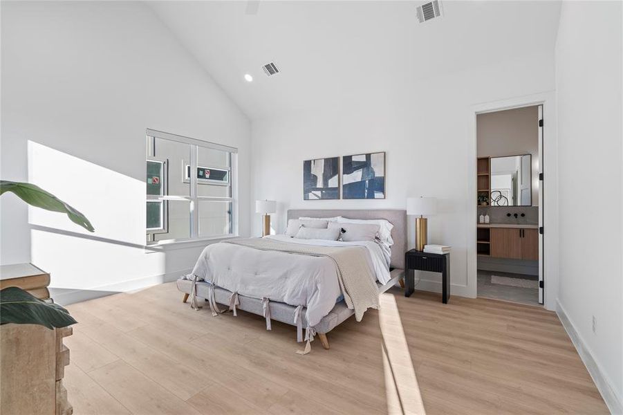 This primary bedroom combines comfort and style, featuring large windows that fill the space with sunlight. The understated design and connection to the en-suite bathroom create a seamless and restful atmosphere.